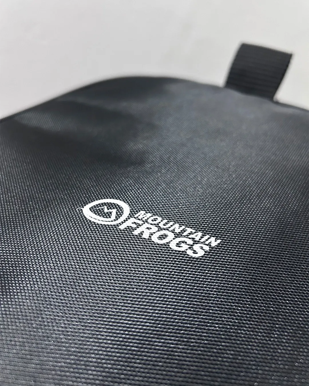 Macro close-up shot of the premium water-resistant polyester fabric texture featuring the crisp white Mountain Frogs brand logo print.